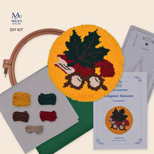 Muijo Atelier DIY Kit for Chapter Autumn, featuring a completed circular punch needle coaster design with a maple leaf and eye glasses, a wooden hoop, yarn balls, a pattern passport, and a punch needle on a light beige background.