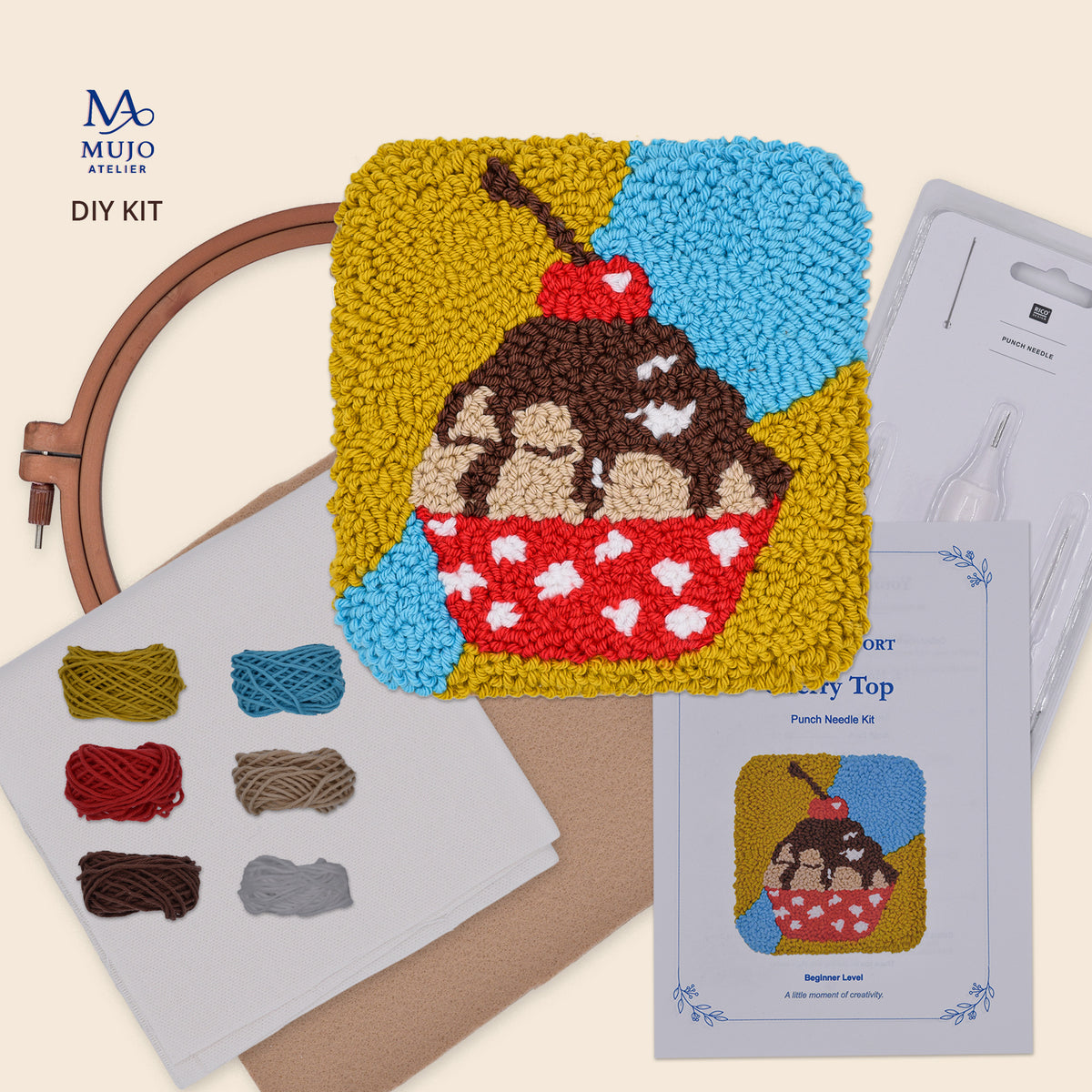 Cherry Top DIY punch needle kit featuring a handmade chocolate cupcake coaster with red cherry, colourful yarn, cotton fabric, embroidery hoop, punch needle, felt backing and Mujo Passport.