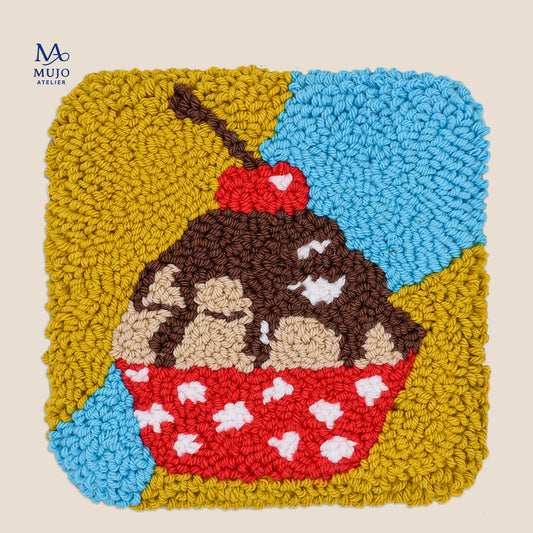 Cherry Top punch needle coaster featuring a chocolate cupcake with cream filling, red polka-dot wrapper and cherry on top, against a yellow and blue background.