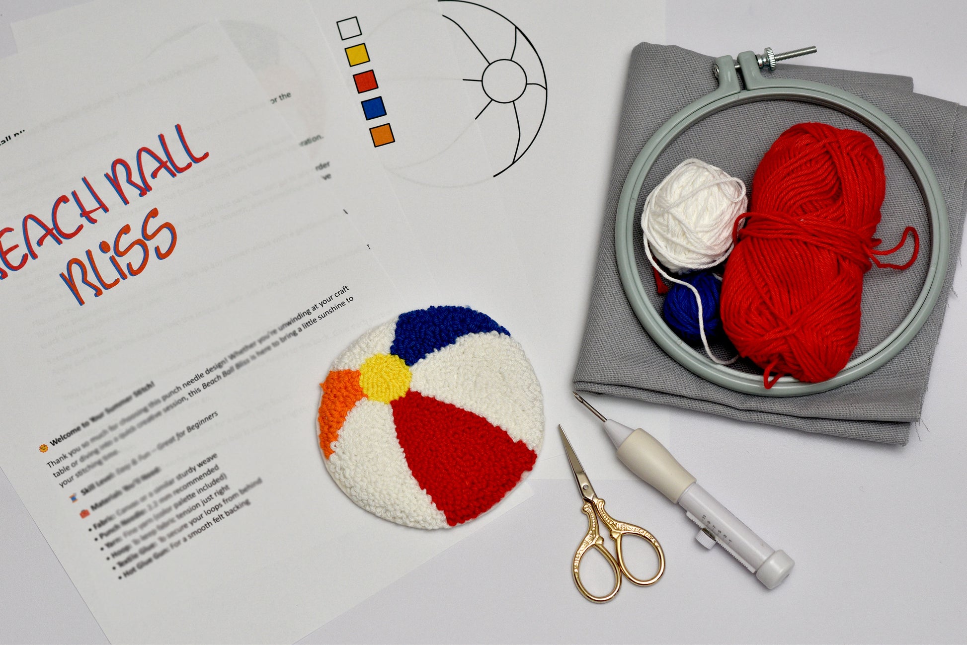 Embroidery hoop with red yarn, scissors, and a colorful beach ball design on paper.