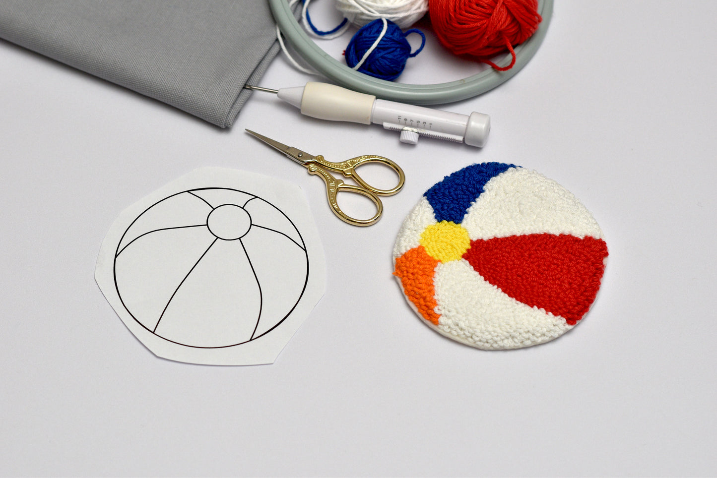 Colorful embroidered beach ball design on a white surface with embroidery tools.
