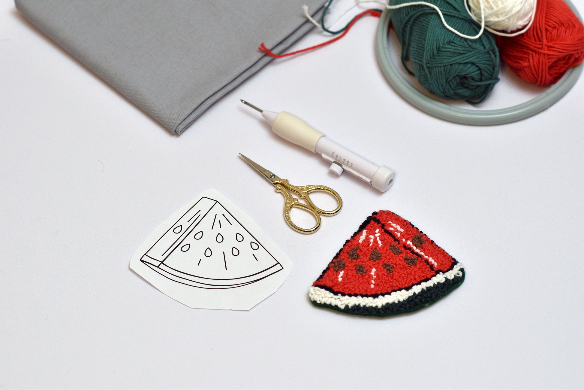 Handmade watermelon slice brooch with sewing tools and yarn on a light surface