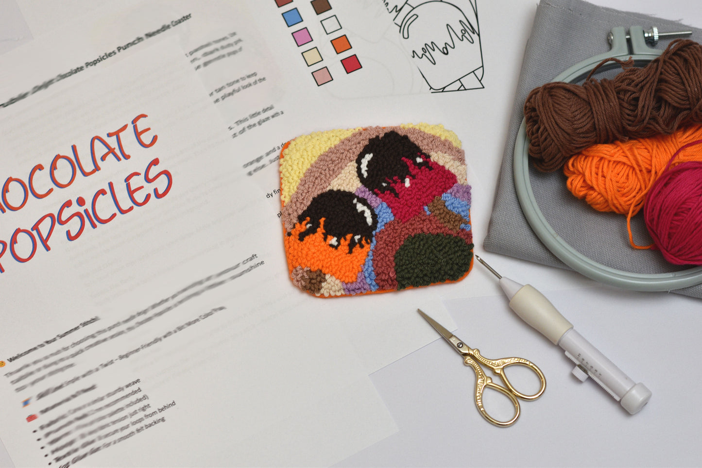 Colorful embroidered patch of people on a white surface with yarn and sewing tools.