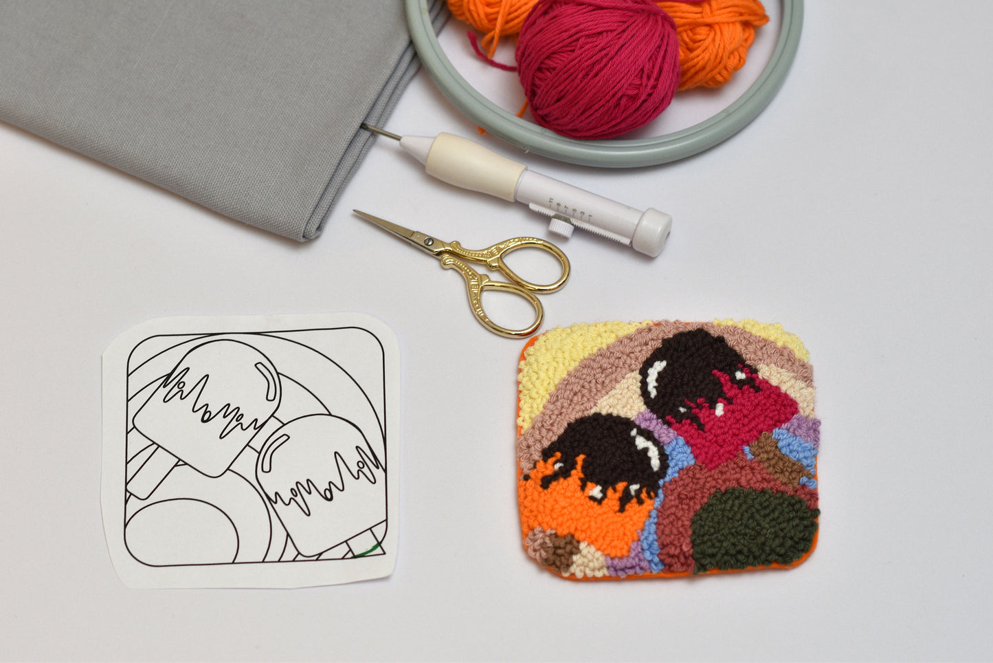 Embroidery hoop with yarn, scissors, and a partially completed embroidered square on a white surface.