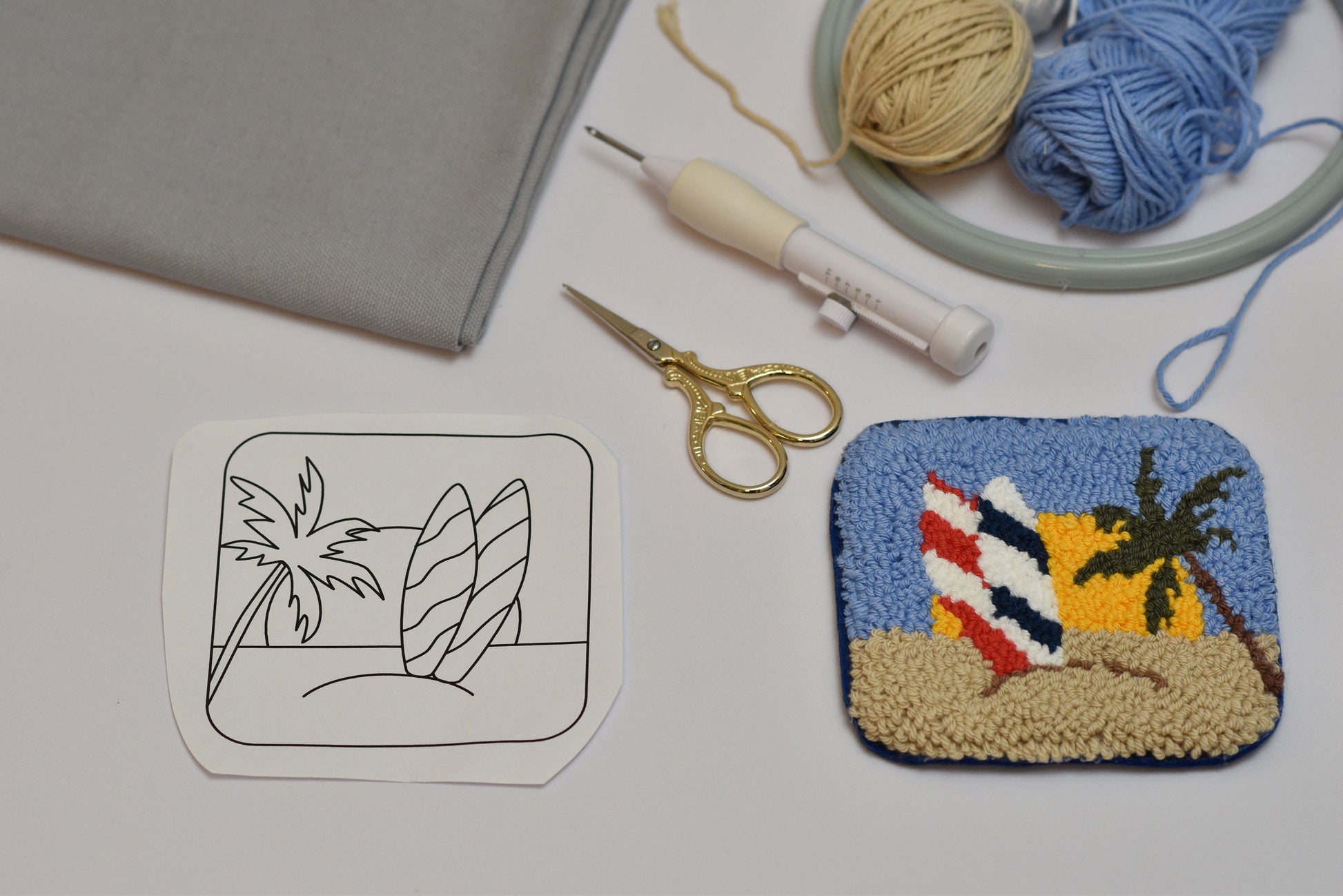 Embroidery hoop with colorful beach-themed fabric piece, scissors, and thread on a light surface.