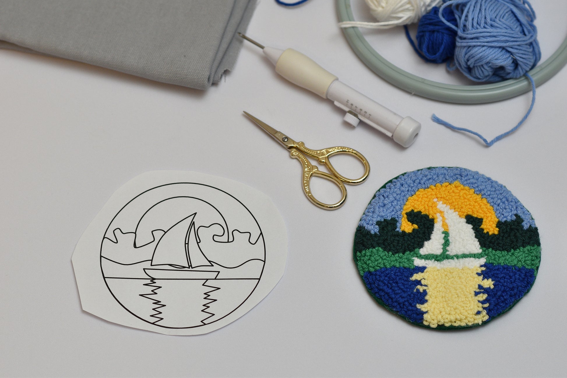 Embroidery hoop with yarn, scissors, and embroidered sailboat design on a white surface