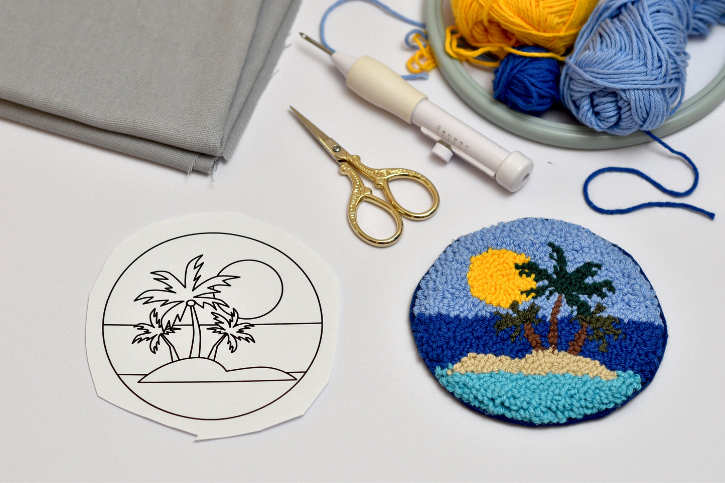 Embroidery hoop with palm tree design, scissors, and yarn on a white surface