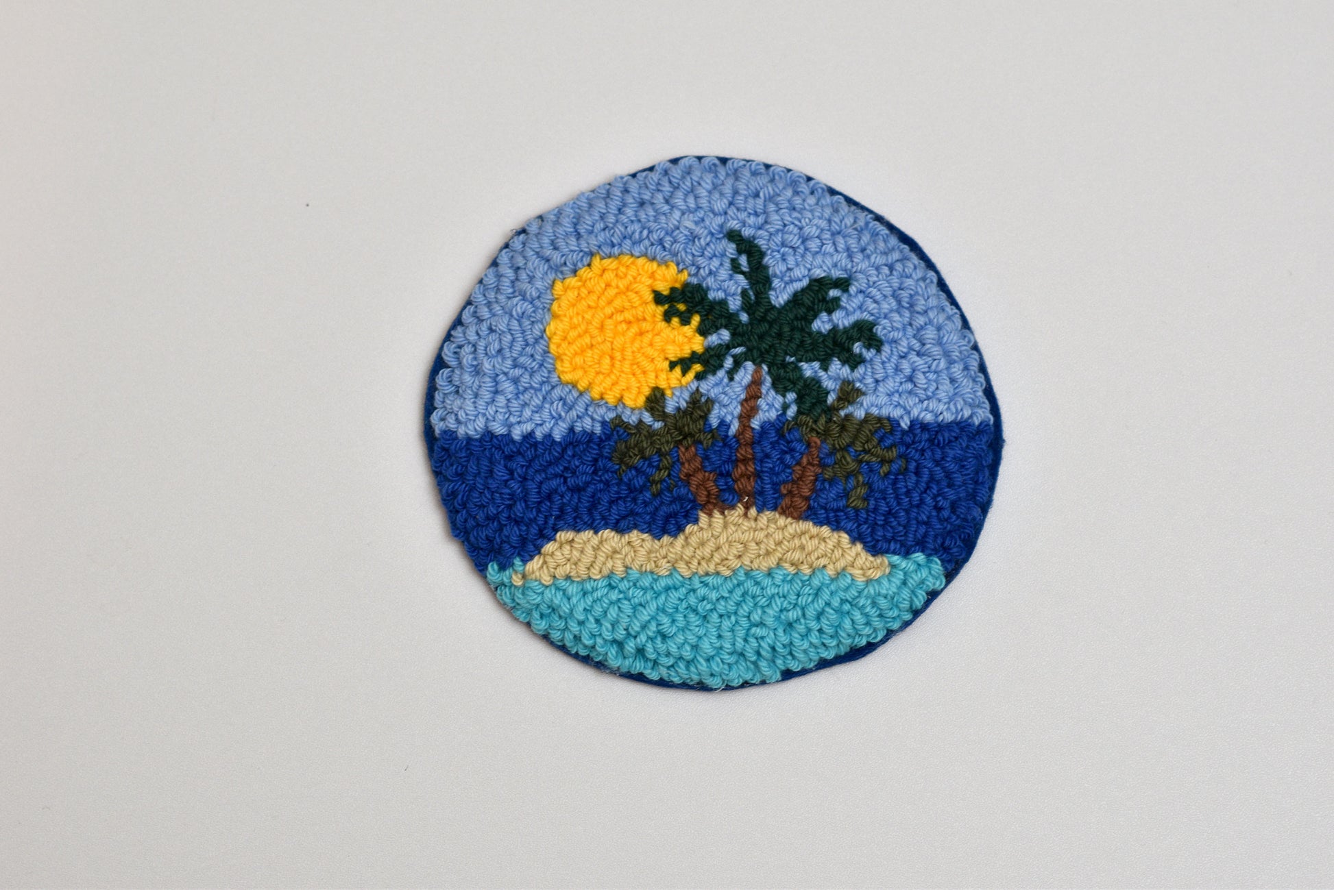 Circular patch with a tropical scene featuring palm trees and a sun on a gray background