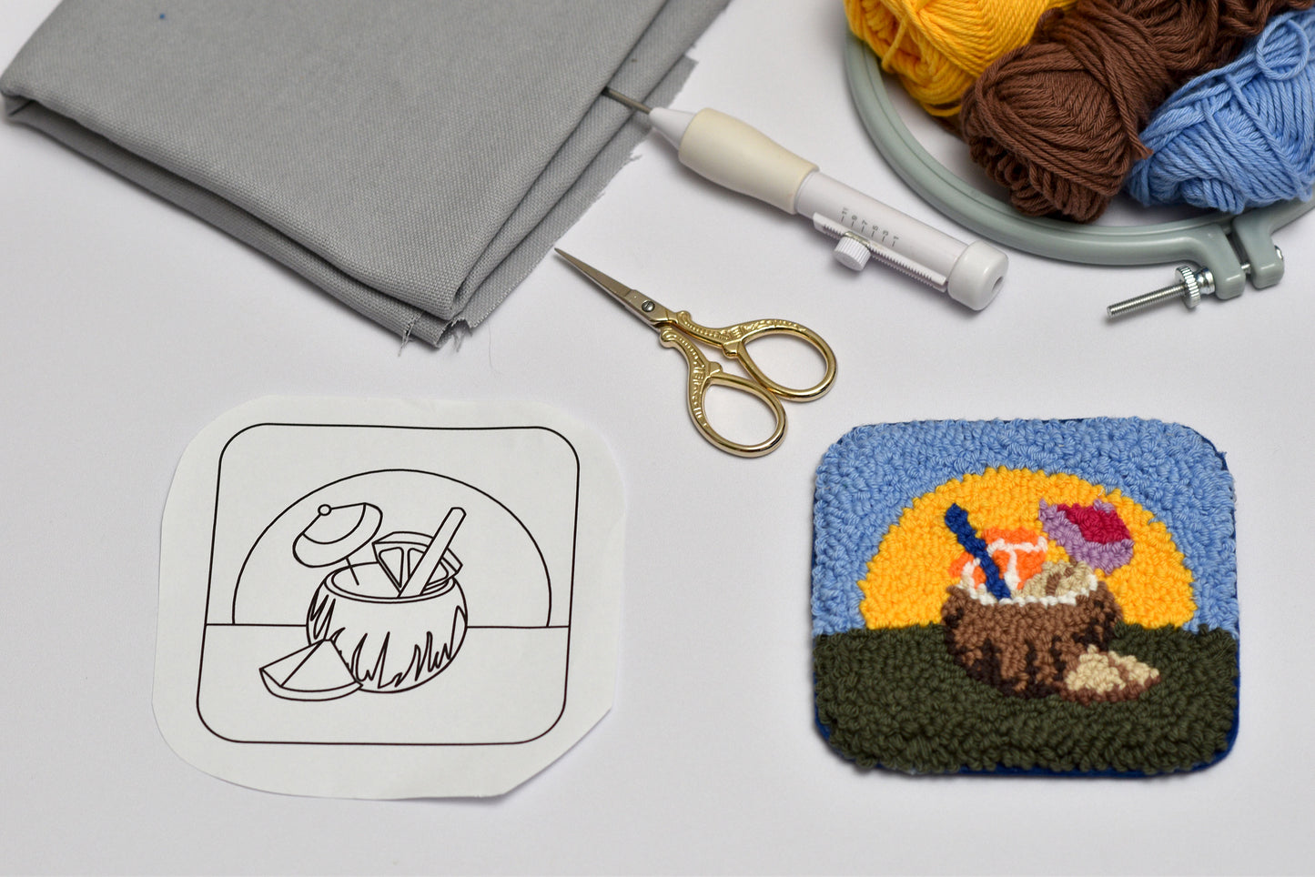 Handmade coaster with a sunset design, scissors, and yarn on a table.