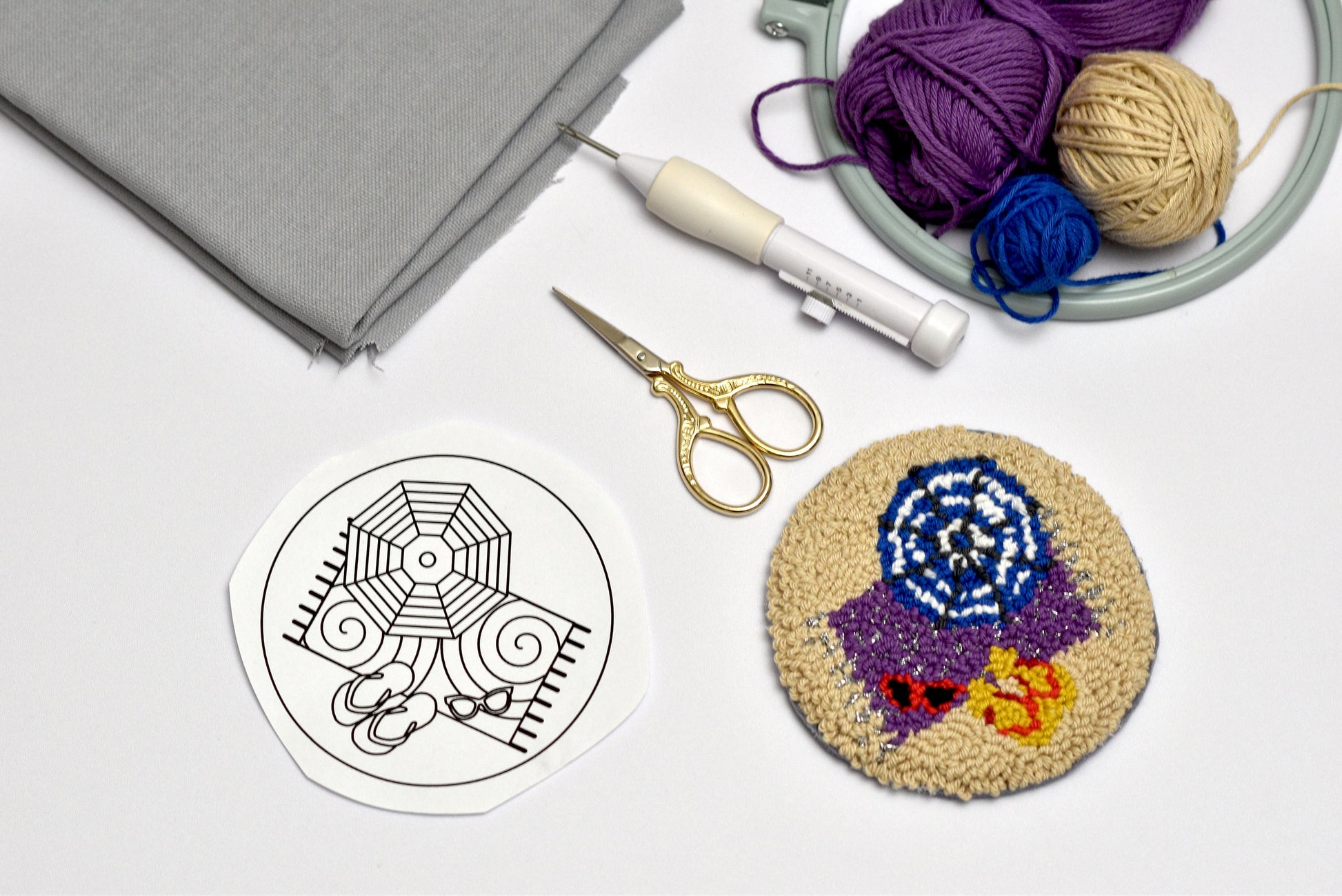 Handmade woven coaster with colorful design next to yarn and knitting tools on a light surface.