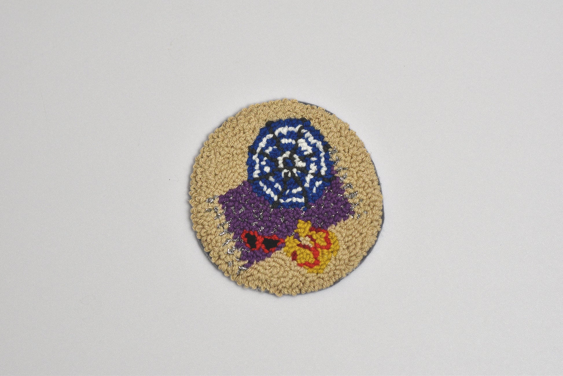 Round woven coaster with a beach towel design on a light gray background