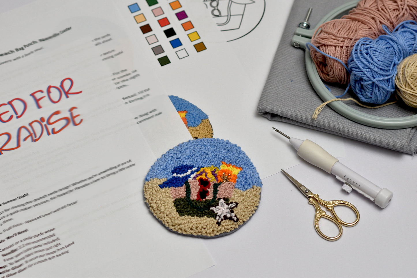 Embroidery hoop with a completed design, yarn, scissors, and pattern sheet on a table.