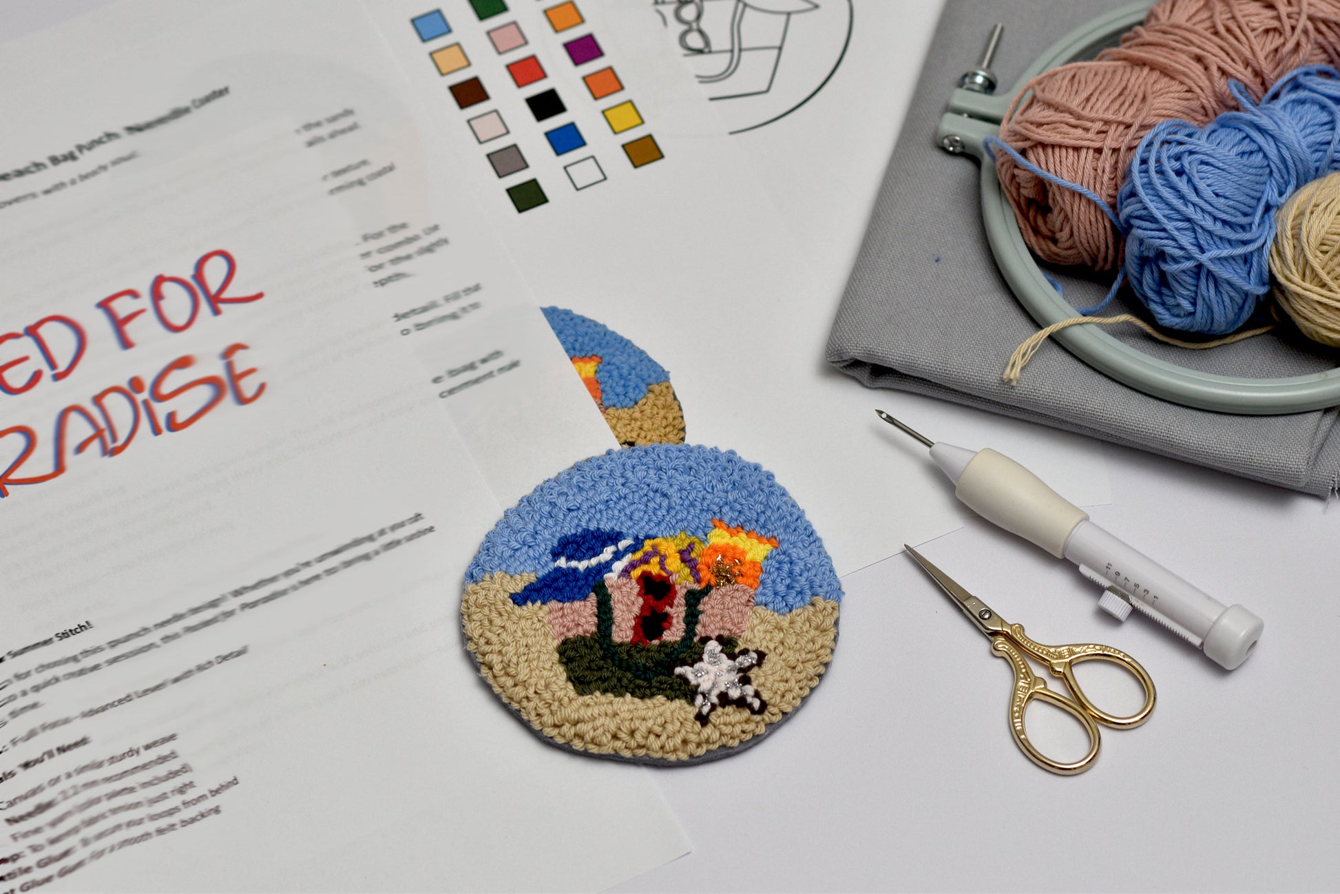Embroidery hoop with a completed design, yarn, scissors, and pattern sheet on a table.