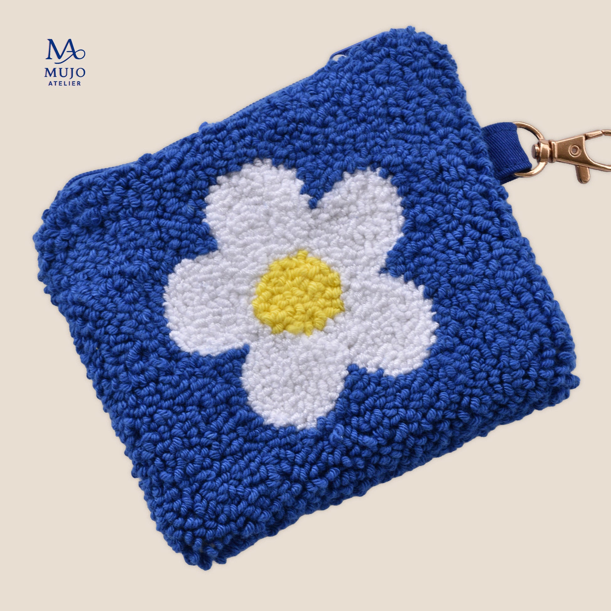 Punch needle coin purse in cobalt blue with a large white daisy and yellow center, finished with a zipper and gold clasp on a soft cream background.