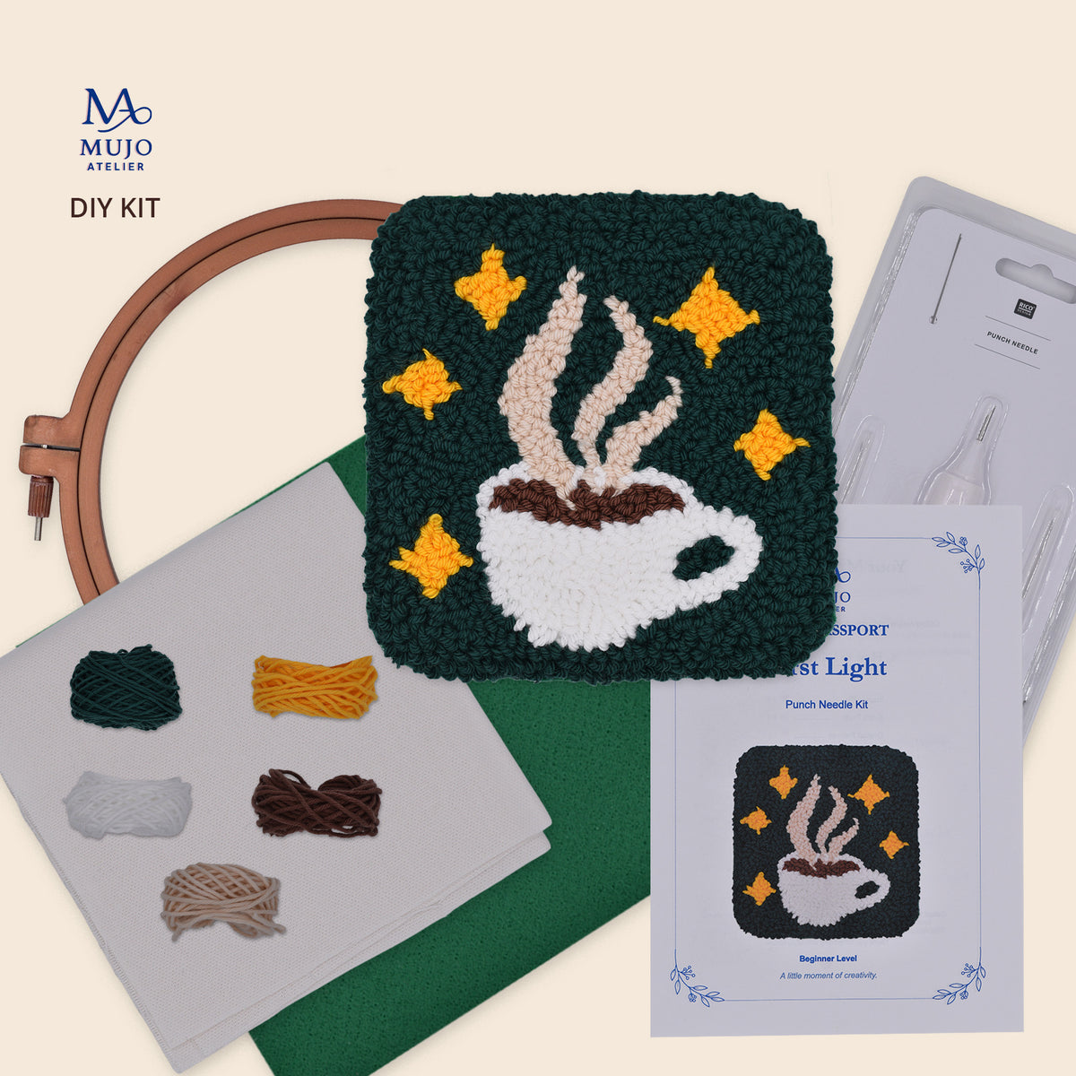 First Light punch needle DIY kit featuring a handmade steaming coffee cup coaster with yellow stars on a dark green background, embroidery hoop, punch needle, five yarn colours, cotton fabric, felt backing and Mujo Passport.