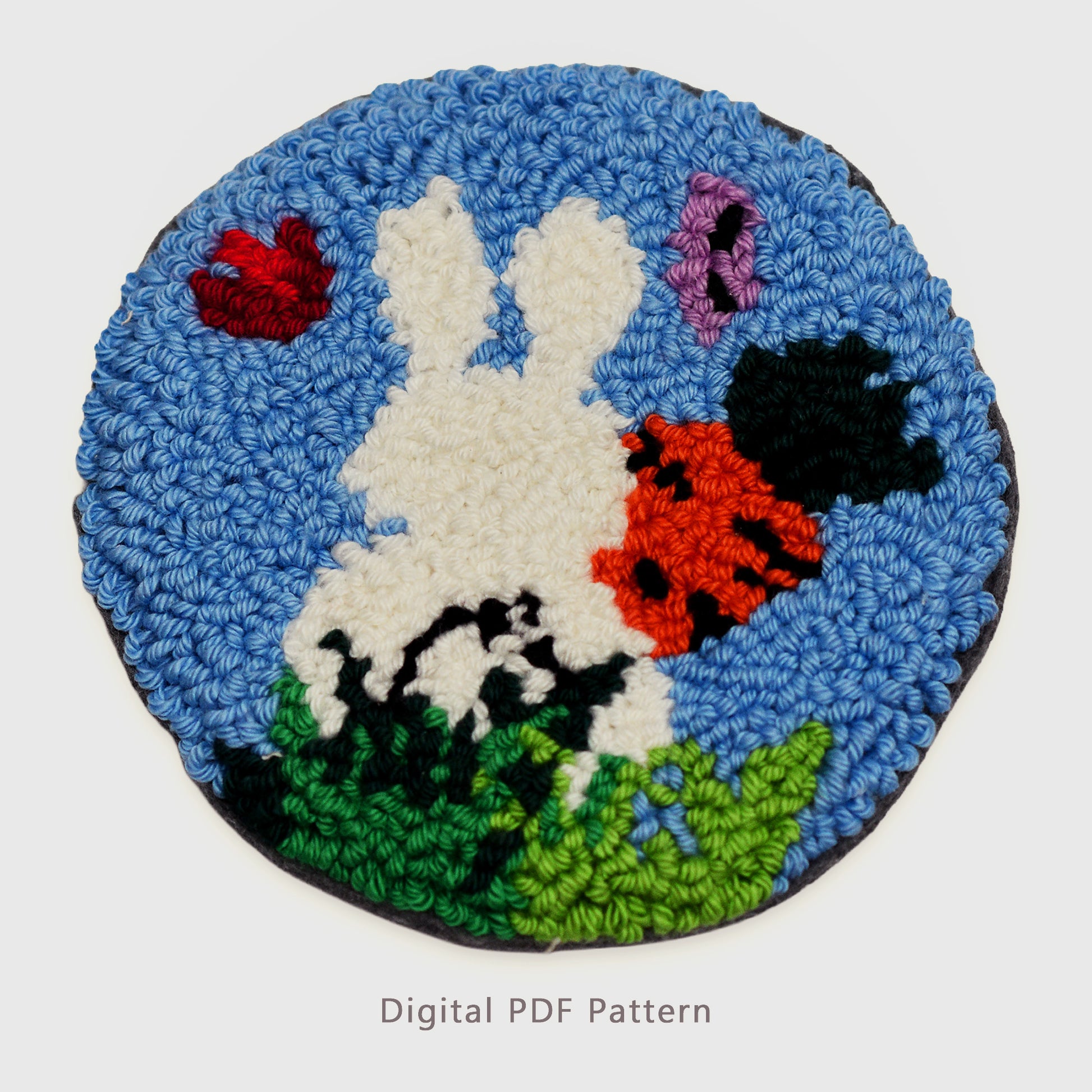 Punch needle digital PDF pattern featuring a bunny from behind holding a carrot in a grassy field with two butterflies on a blue background coaster design