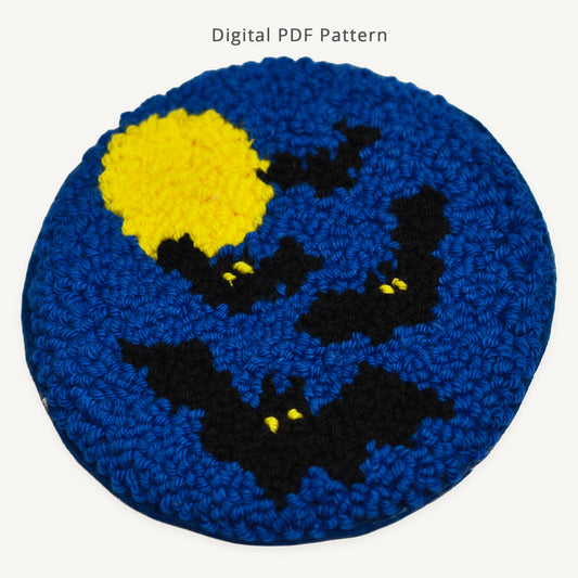 Punch needle coaster pattern featuring black bats flying across a deep blue night sky with a bright full moon. Digital PDF punch needle pattern for creating a Halloween-themed coaster with detailed instructions and printable template.