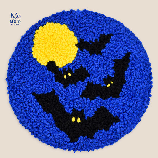 Moon Watchers punch needle coaster featuring black flying bats with glowing yellow eyes, a full yellow moon and deep blue night sky.