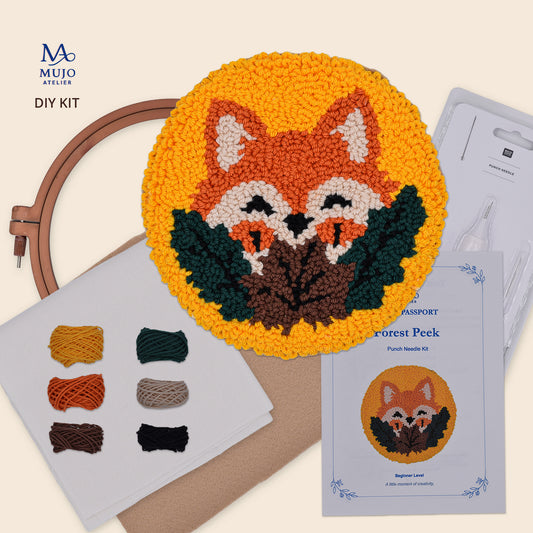 Mujo Atelier DIY Hook and Loop (Punch Needle) Kit for crafting a fox head coaster The image displays the completed round yellow coaster with a detailed orange, white, and green fox design, alongside the wooden embroidery hoop, fabric samples, a passport-style template, and the product booklet on a light beige background.