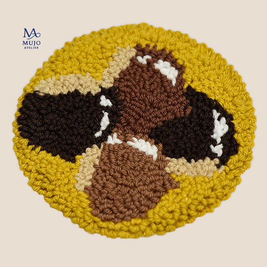 Round punch needle coaster featuring a cozy autumn chestnut design in warm brown, cream and mustard yellow yarn, handmade with textured loops on a neutral background.