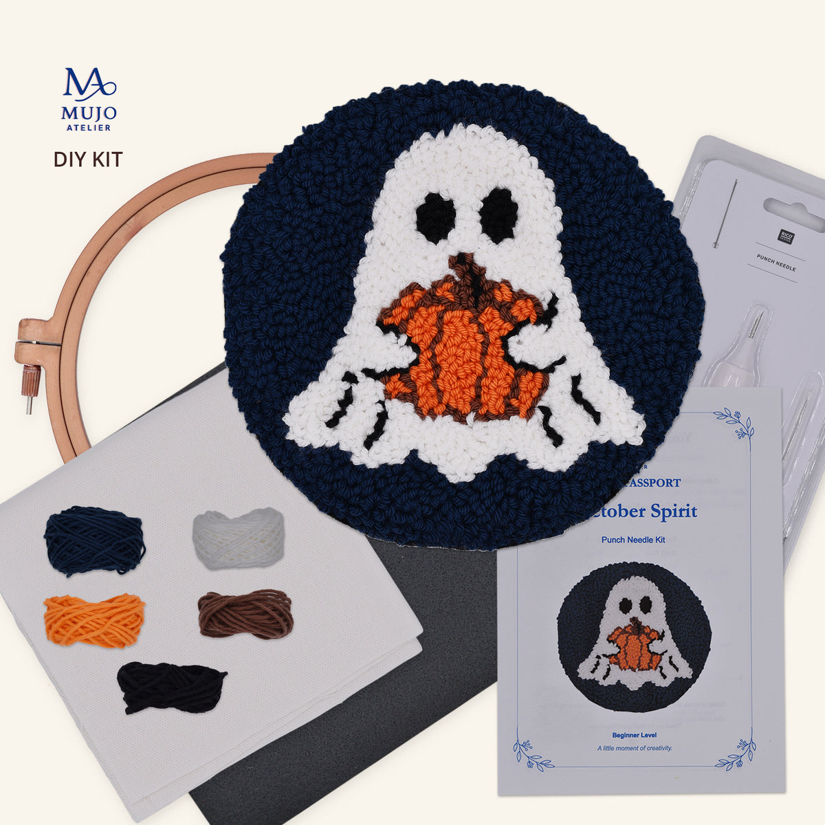 Mujo Atelier DIY punch needle kit featuring a completed Halloween ghost and pumpkin coaster, an embroidery hoop, yarn skeins, a package of thread, and a registration card on a light cream background.