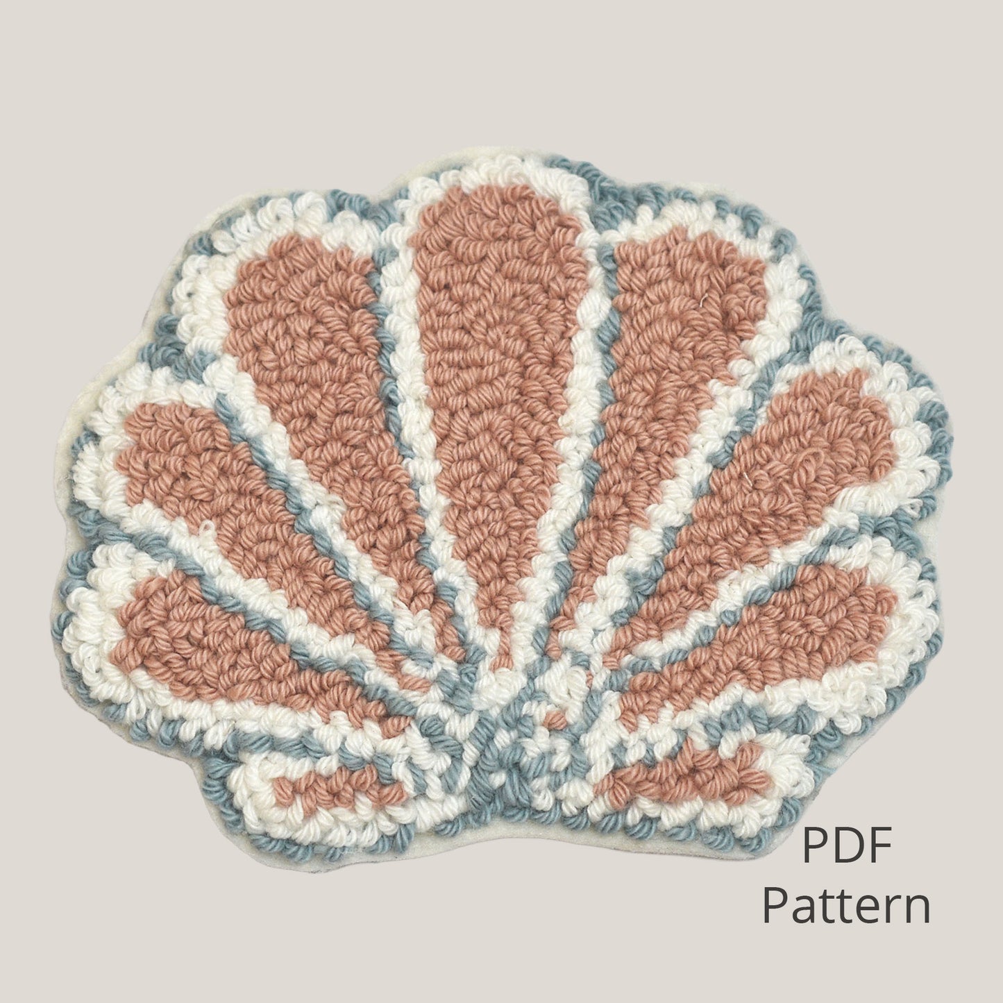 Seashell punch needle coaster PDF pattern displayed on a soft warm grey background, featuring a handmade textured shell design in blush pink, cream, and muted blue, beginner-friendly digital download.