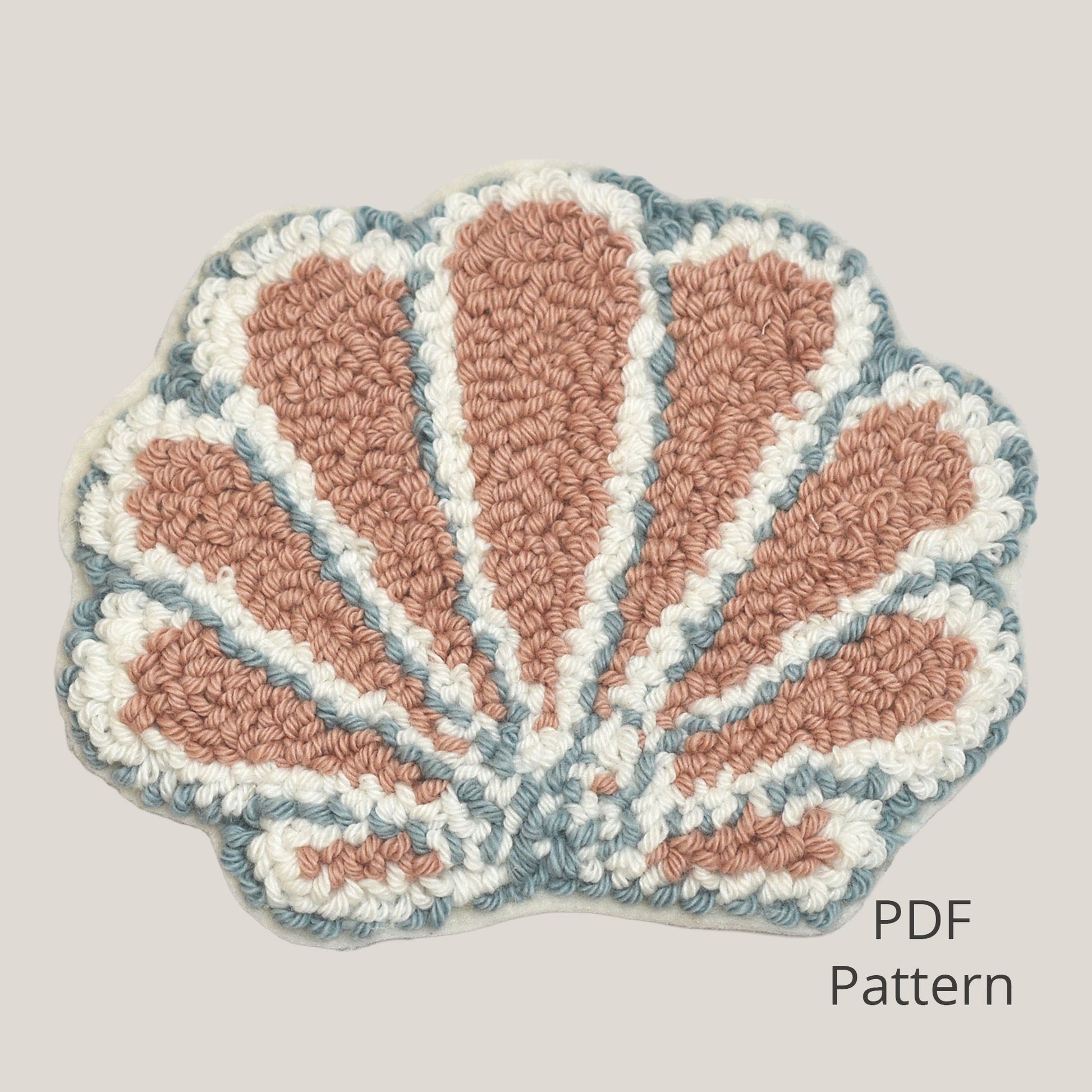 Seashell punch needle coaster PDF pattern displayed on a soft warm grey background, featuring a handmade textured shell design in blush pink, cream, and muted blue, beginner-friendly digital download.