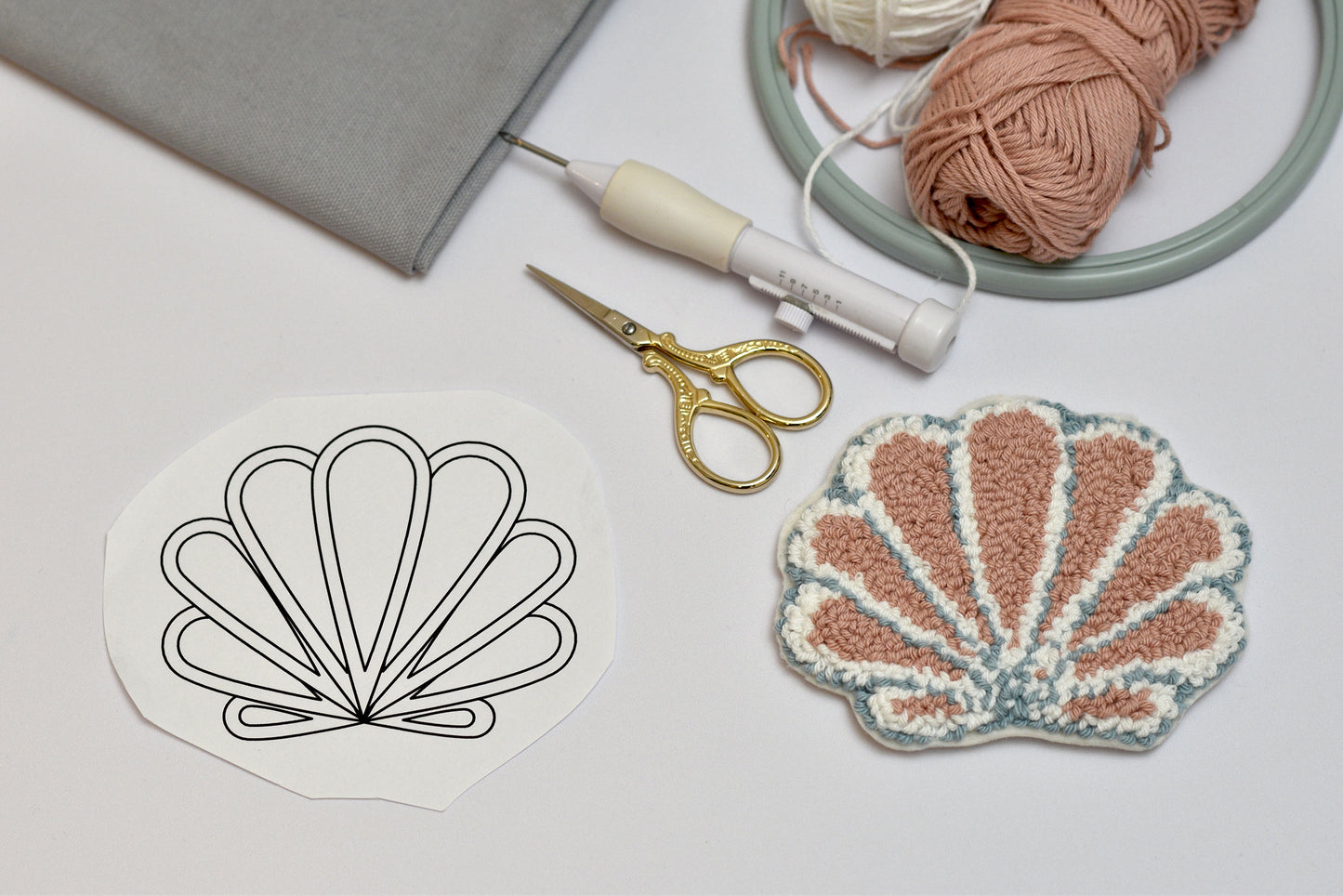 Seashell design template with embroidered seashell, scissors, and yarn on a light surface