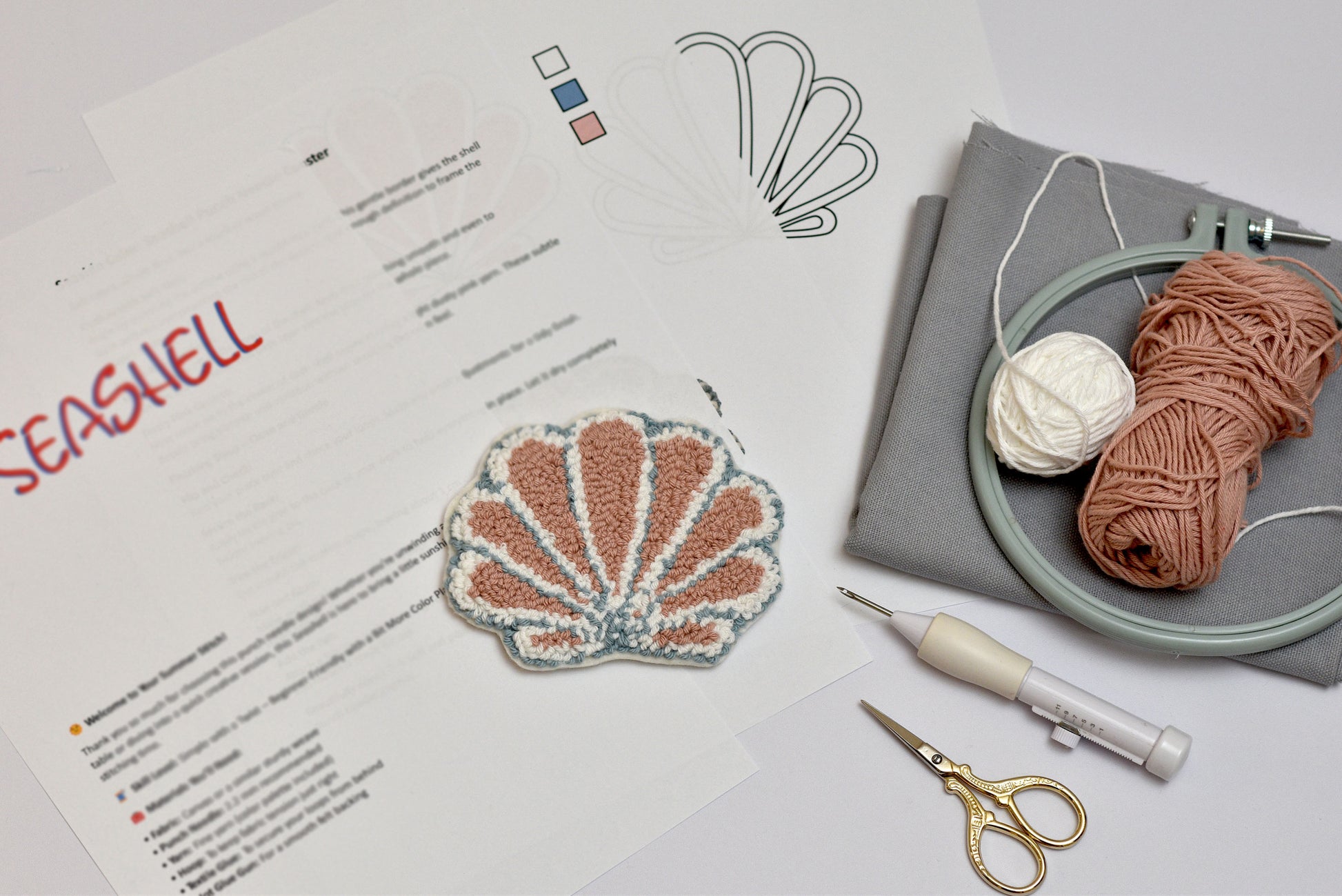 Seashell embroidery design with yarn, scissors, and an embroidery hoop on a table.