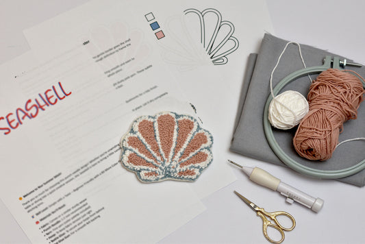 Seashell embroidery design with yarn, scissors, and an embroidery hoop on a table.