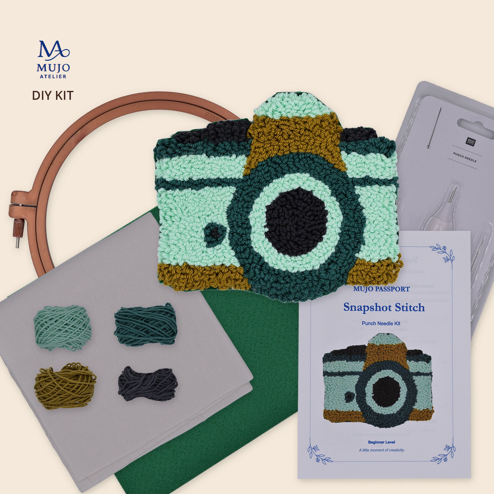 Punch needle DIY kit for a retro camera coaster, featuring the finished Snapshot Stitch design with yarn, fabric, felt, embroidery hoop, punch needle and printed instructions.