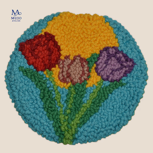 Punch needle pattern featuring three colorful tulips in red, purple and pink with green stems and leaves on a turquoise blue background.