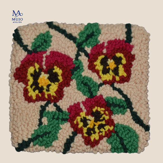 Punch needle pattern featuring three red viola flowers with yellow and dark centers, green leaves and winding stems on a warm cream background.