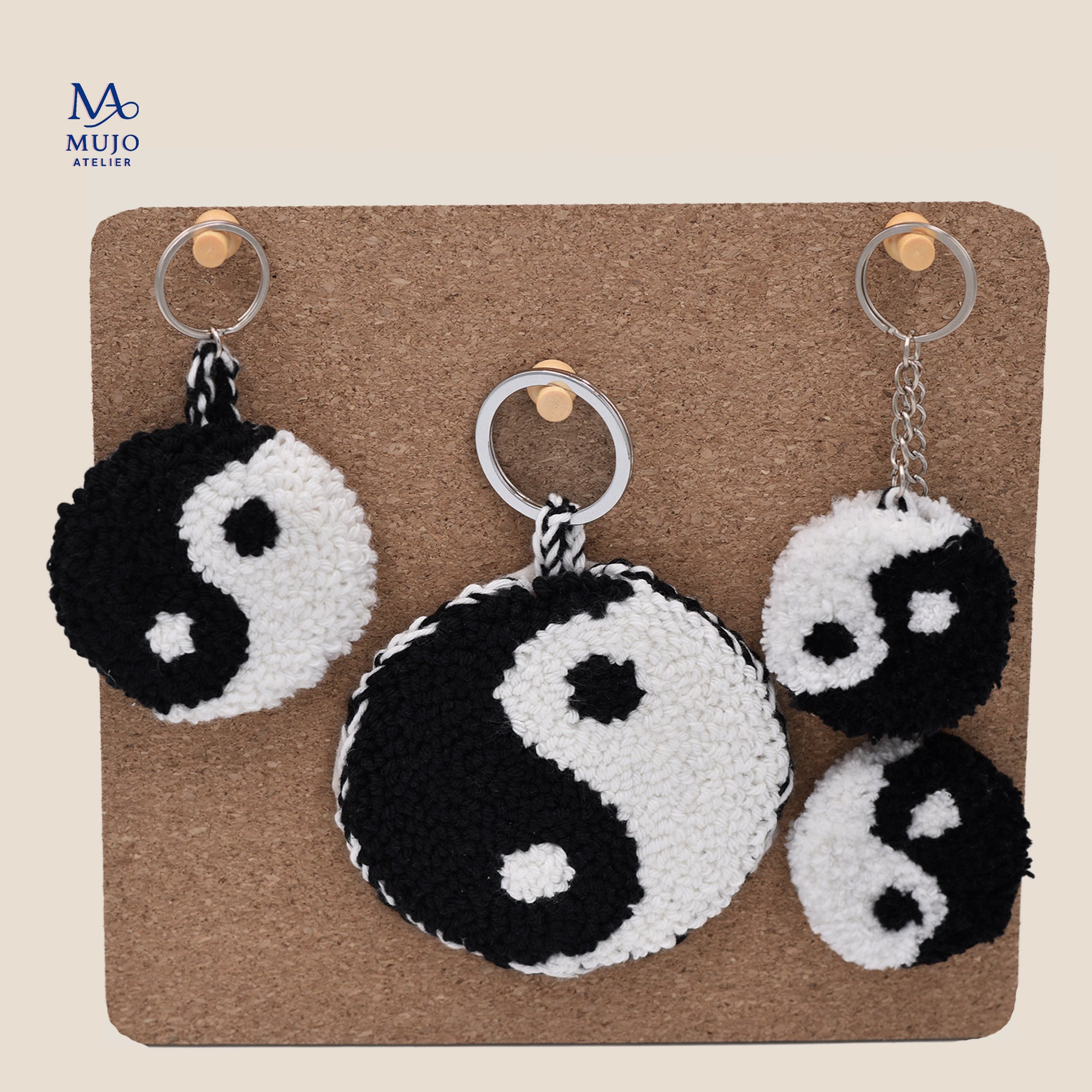 Yin yang punch needle keychain pattern displayed in three sizes, black and white handmade textured design shown on cork board background