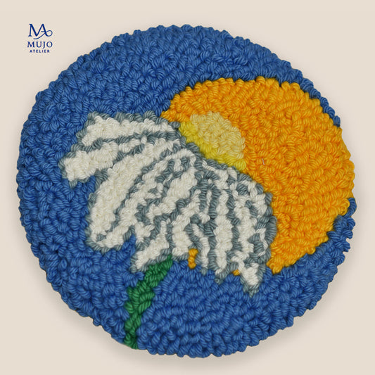 Punch needle coaster featuring a large white daisy with grey details in front of a golden yellow sun, with a green stem against a deep blue background.