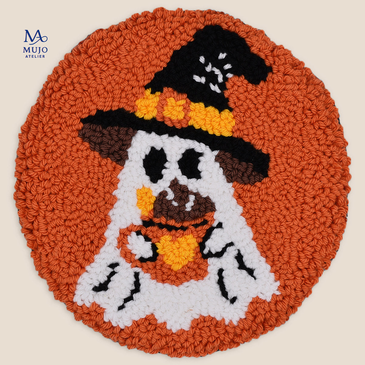 A circular, punch needle coaster featuring a Halloween ghost design. The coaster has a textured orange border, with a ghost motif in white, brown, black, and orange.