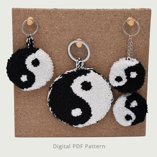 Yin yang punch needle keychain pattern displayed in three sizes, black and white handmade textured design shown on cork board background