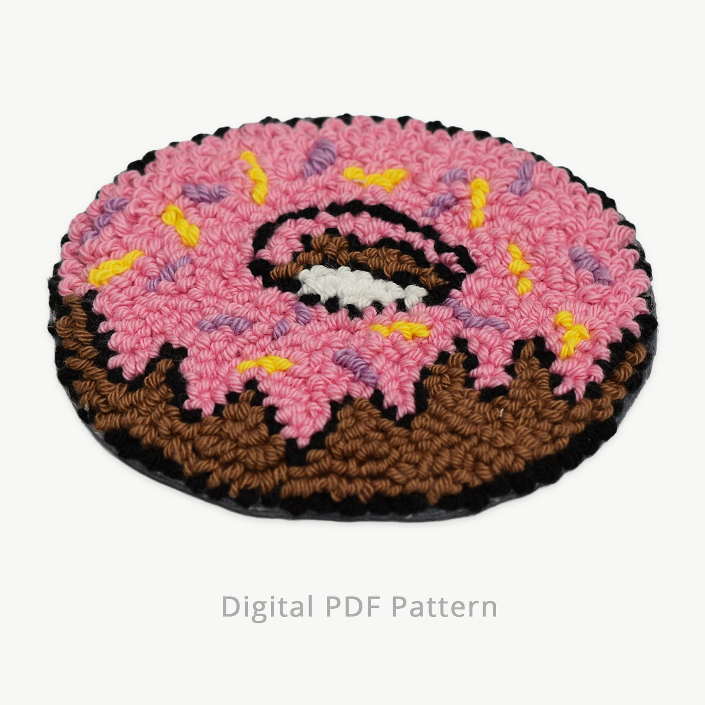 Punch needle donut coaster design with pink icing and sprinkles, shown as a digital PDF pattern on a neutral background
