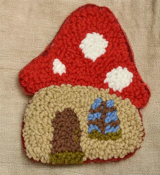 Punch needle mushroom house coaster, handmade red mushroom cottage design on linen background, beginner friendly punch needle pattern